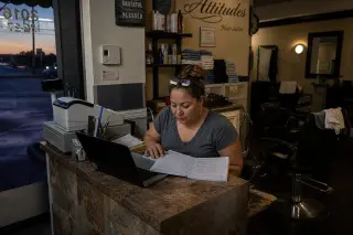hair salon owner in casual clothes checking ledger and laptop at the back counter after closing, soft evening light, authentic and natural atmosphere